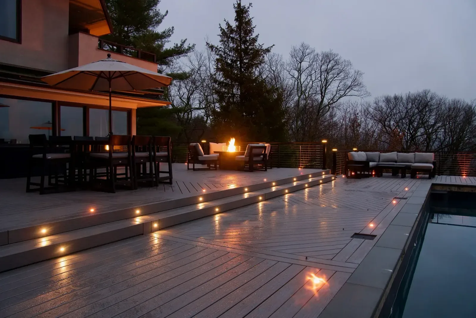 Covered outdoor living space with fire feature and pool at dusk