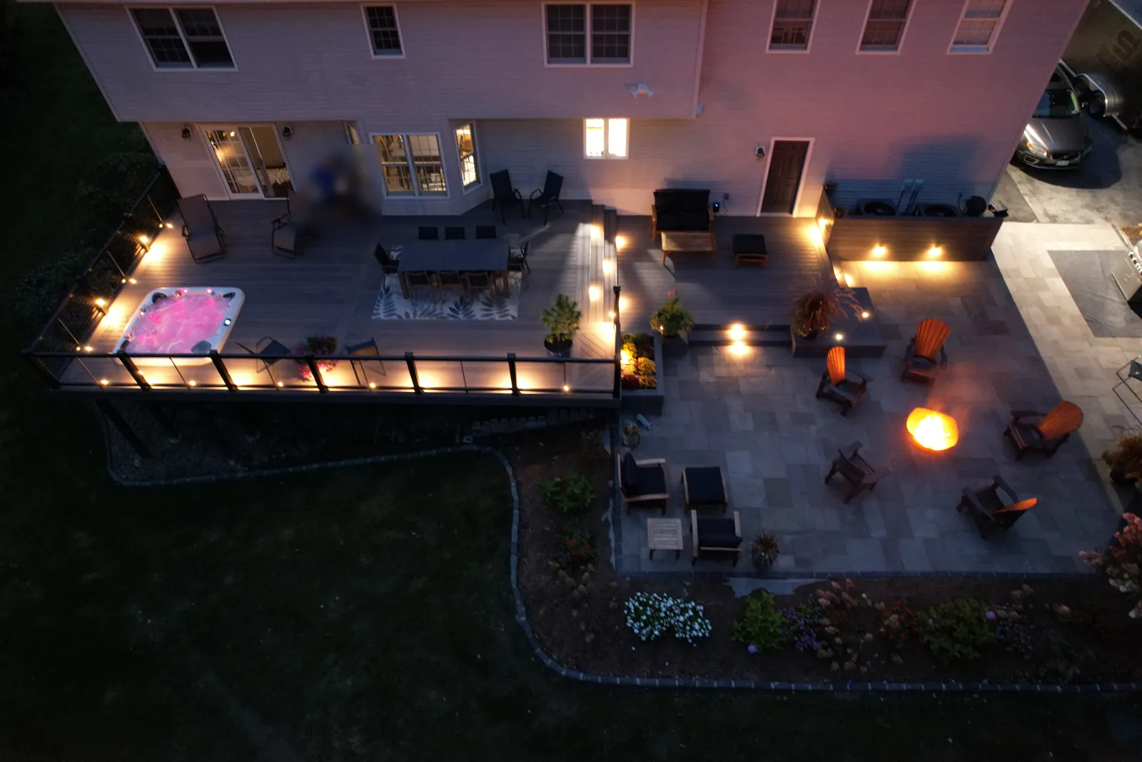 Deck with spa and dining area beside a paver patio and fire pit in the evening