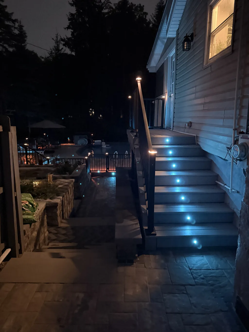 Lit deck stairs with riser lights above a paver walkway