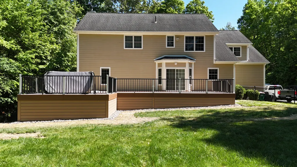 Aerial of a composite deck with a hot tub and black railing behind a tan house