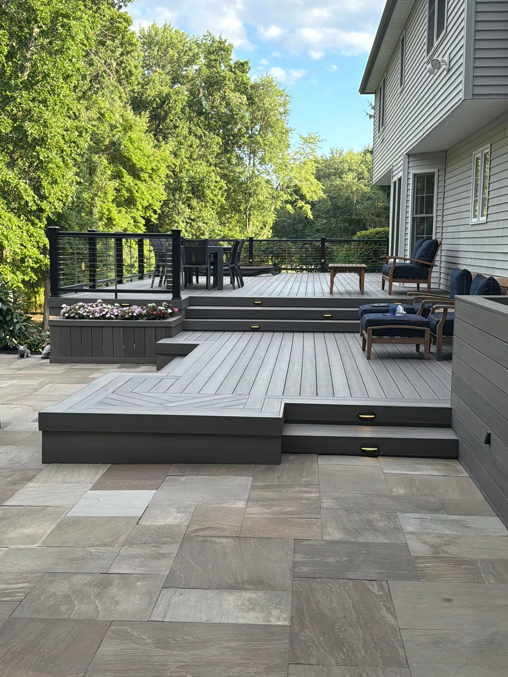 Gray composite deck with herringbone inlay platform, cable railing, and paver patio