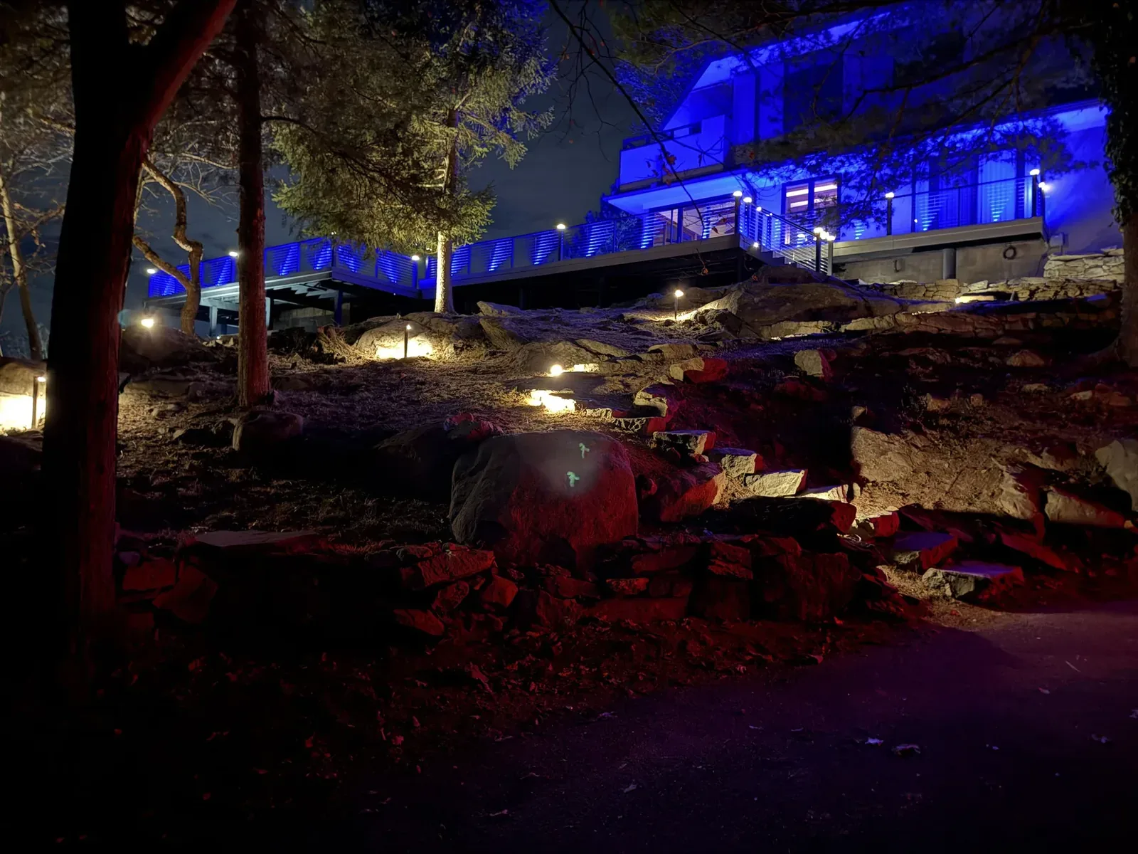 Steep rocky terrain below Hudson Horizon Haven at night — lit stone steps climbing the bluff to the elevated deck structure above