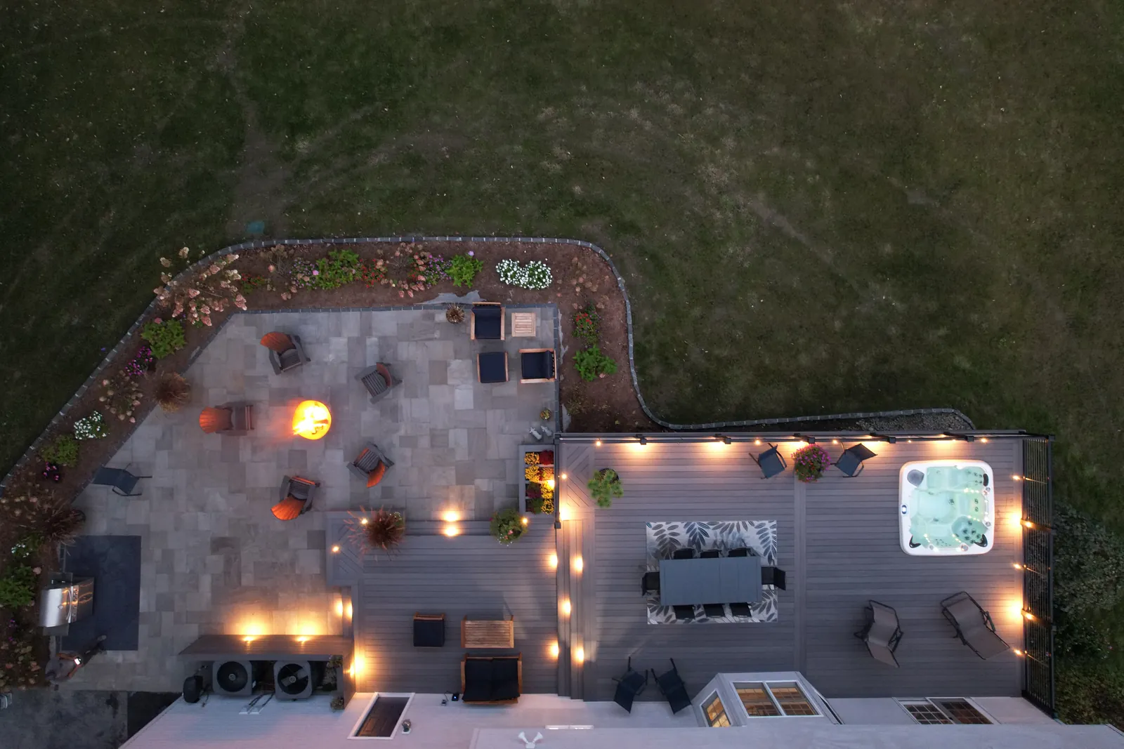 Overhead view of a deck, paver patio and fire pit lit at dusk