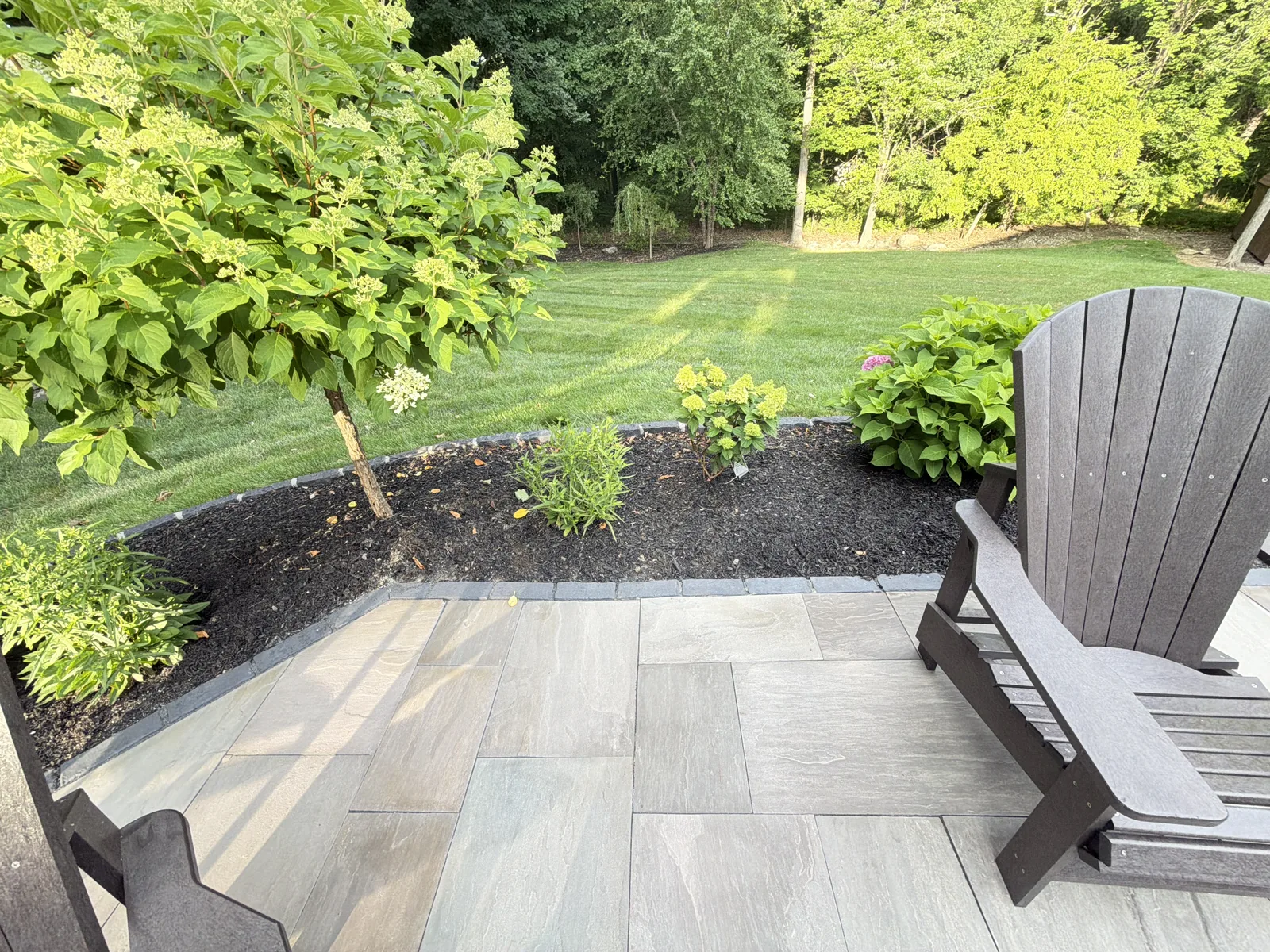 Paver patio with Adirondack chairs beside a landscaped bed