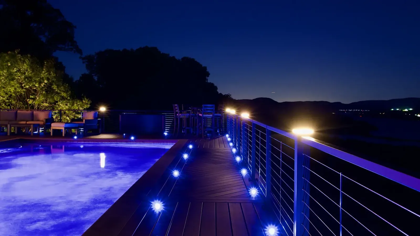 Pool deck with blue lighting and cable railing at night