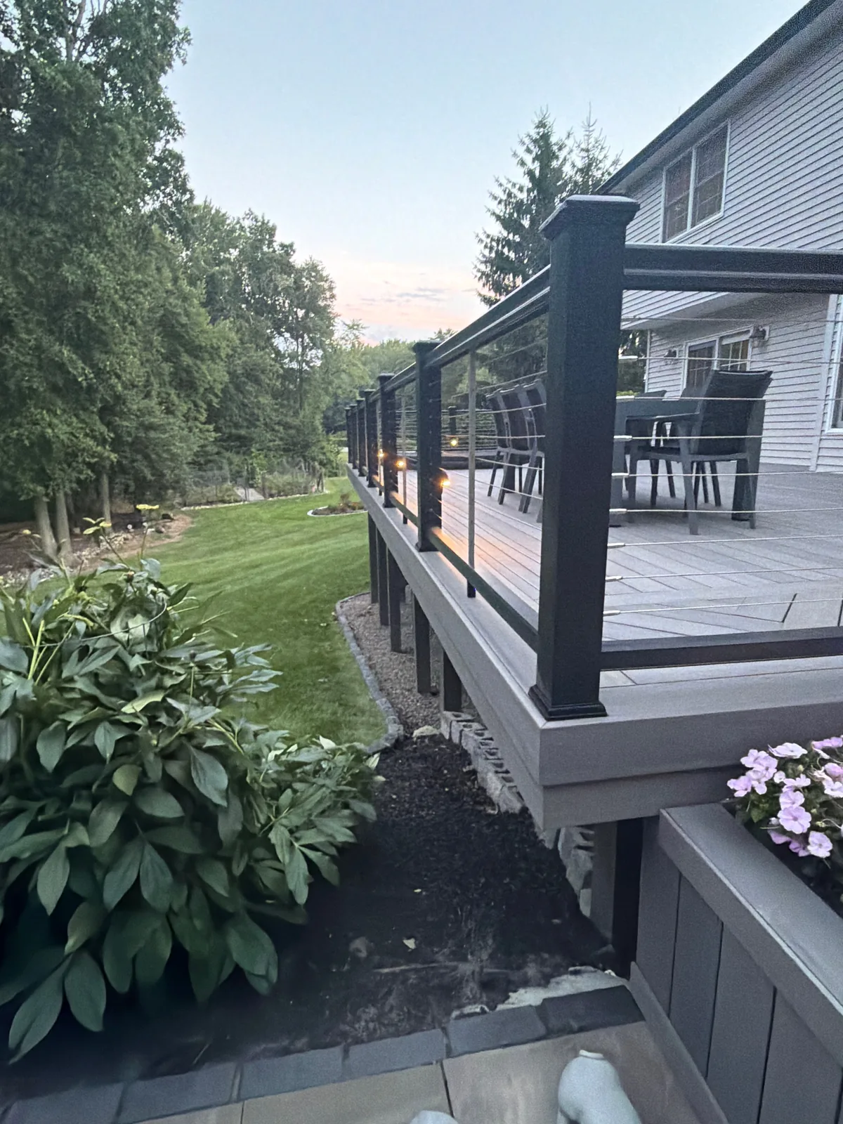 Finished multi-level composite deck at dusk in LaGrange, NY — black posts, cable railing, and post lighting on