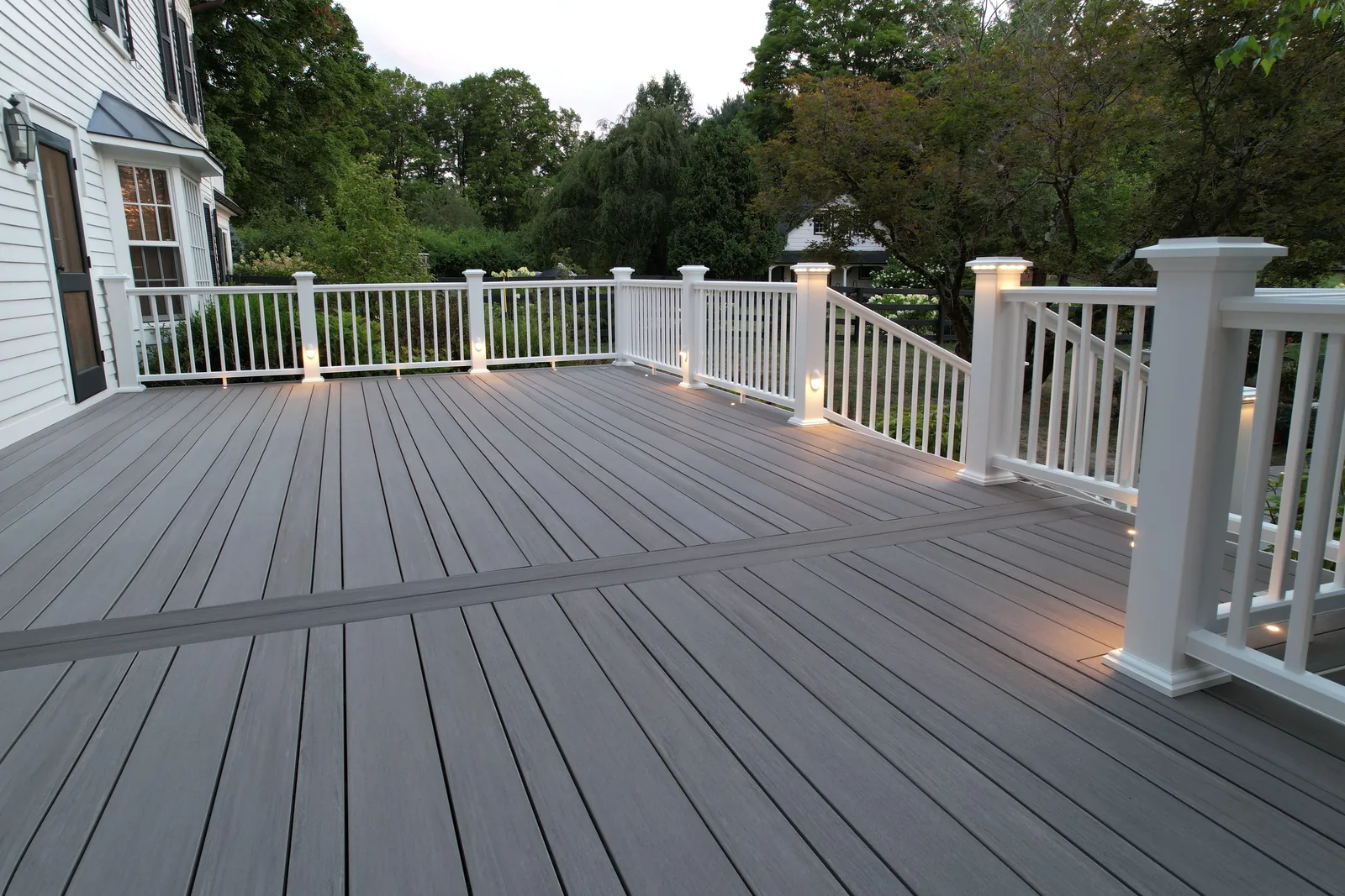 TimberTech deck at dusk with white railing, post-cap and riser lighting, and a picture-frame border