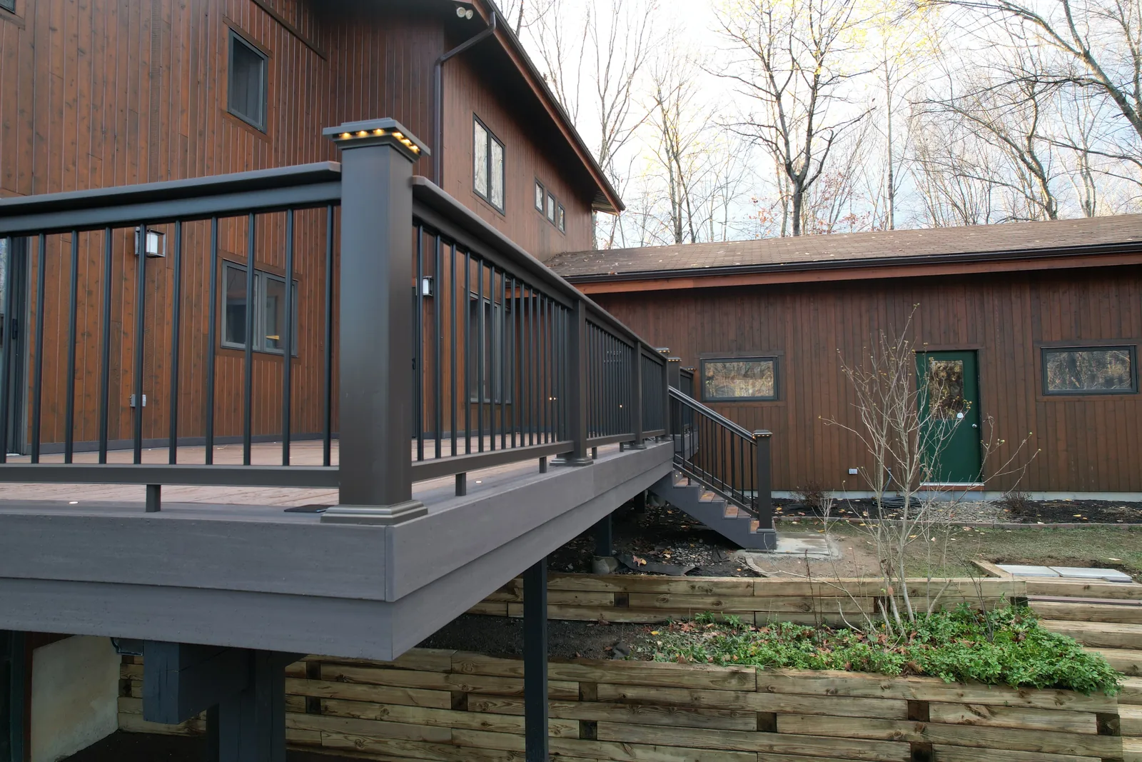 Elevated TimberTech deck with bronze railing and a stair run to grade on a dark-sided home