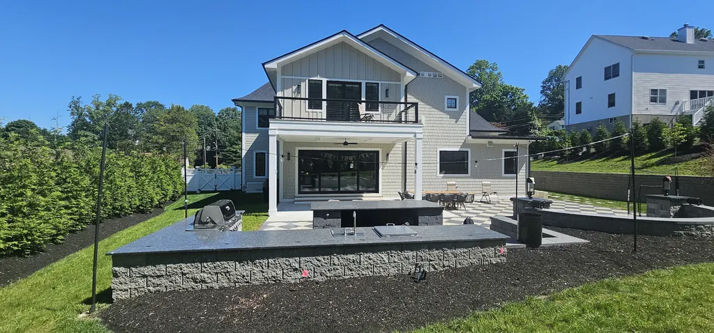 Back of a white house with a cable-rail balcony, a covered patio, a checkerboard paver patio, and an outdoor kitchen