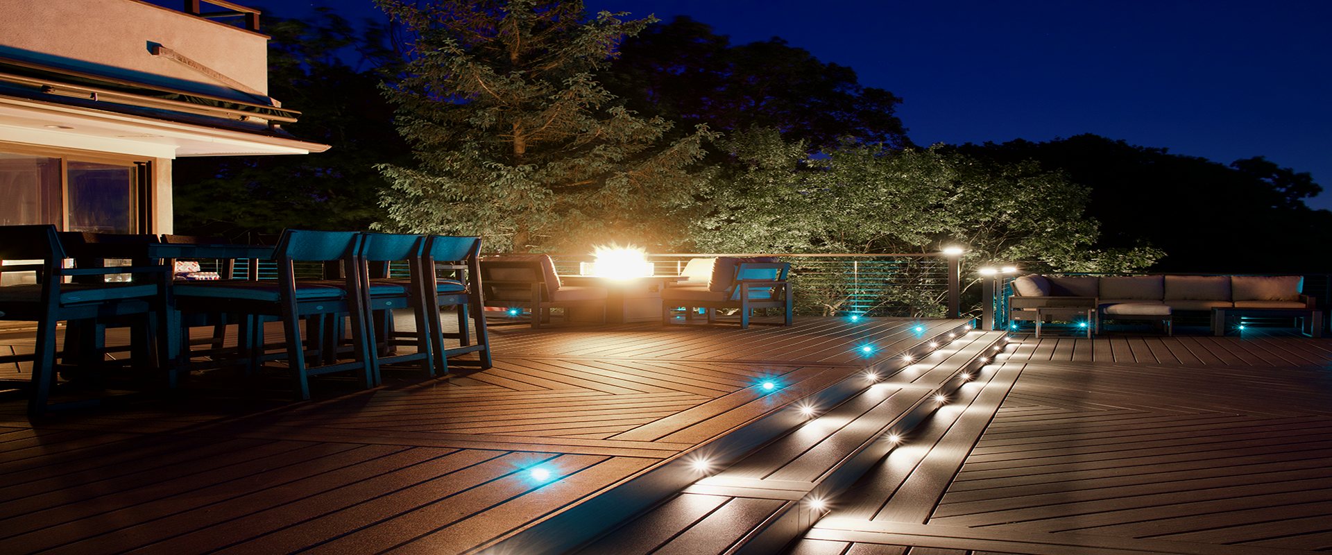 Herringbone Trex deck at night with teal in-deck riser lighting and a fire feature — Pinnacle Decking Hudson Valley NY