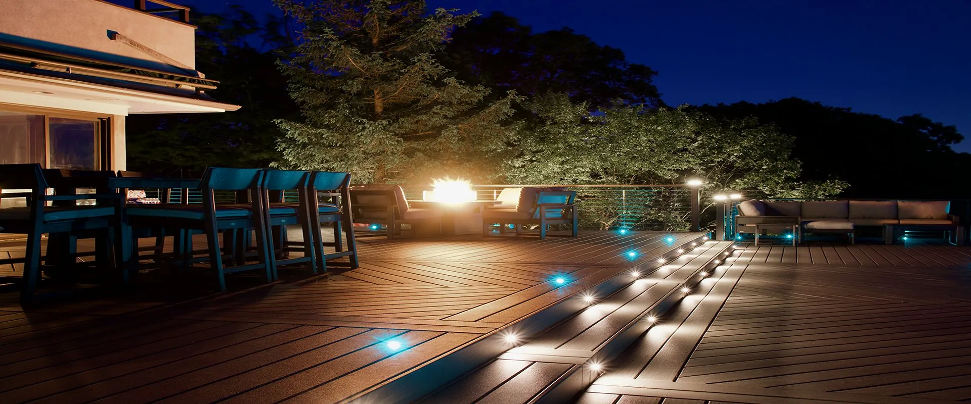 Herringbone Trex deck at night with teal in-deck riser lighting and a fire feature — Pinnacle Decking Hudson Valley NY