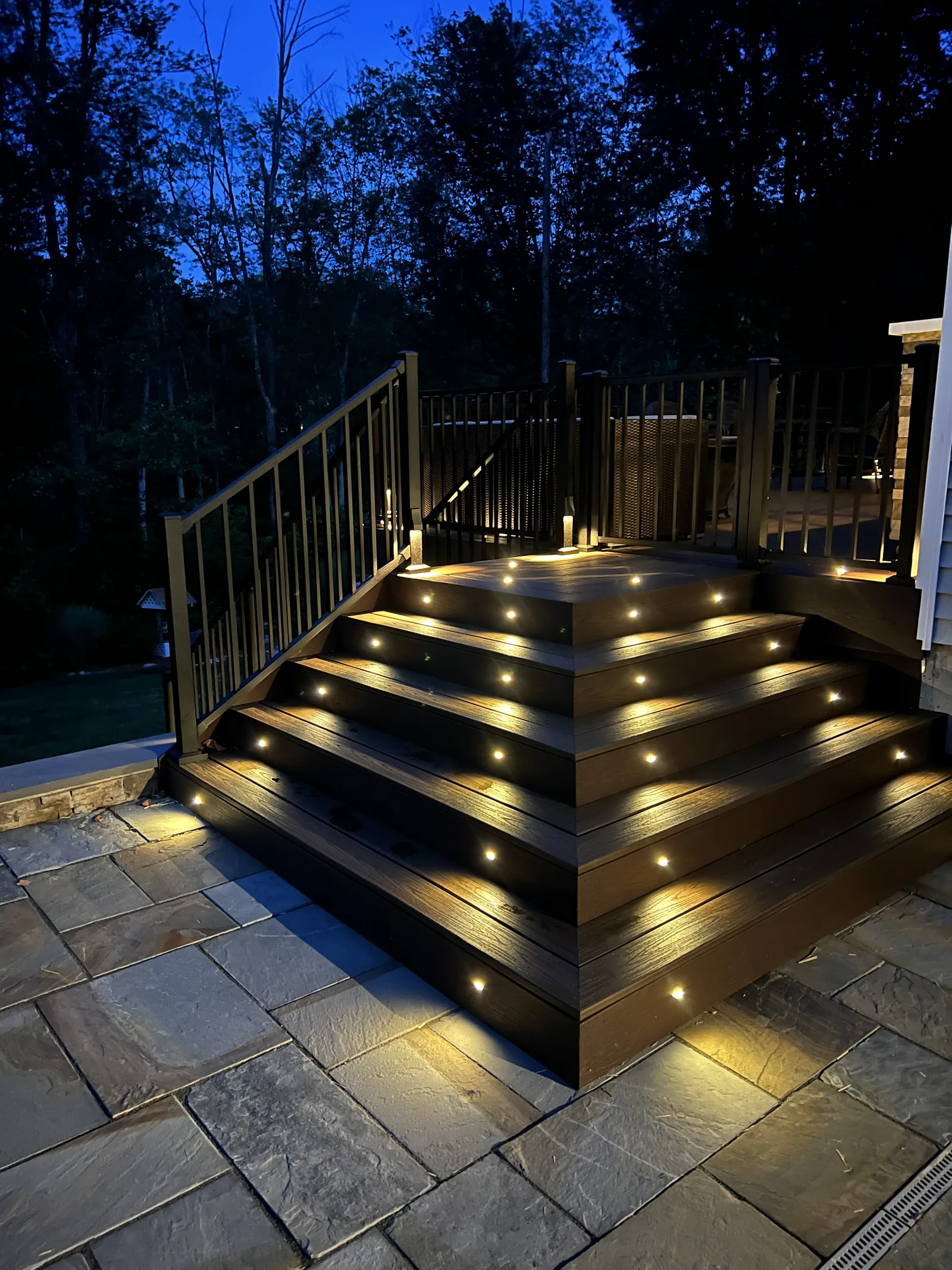 Illuminated deck stairs at dusk over a bluestone patio in the Hudson Valley, NY