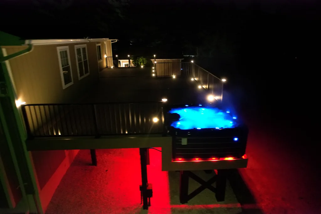 Hot tub on an elevated composite deck with low-voltage railing lights and under-deck accent glow at night