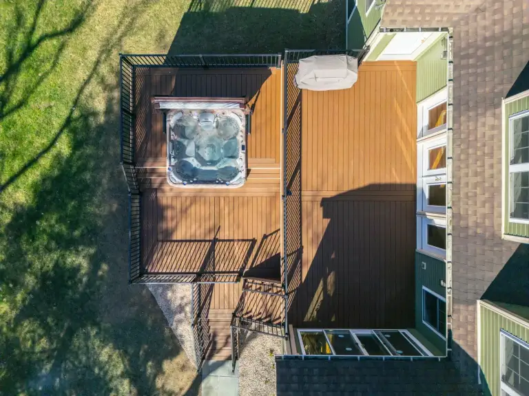 Overhead view of a deck with a hot tub, black railings, and stairs beside a green house