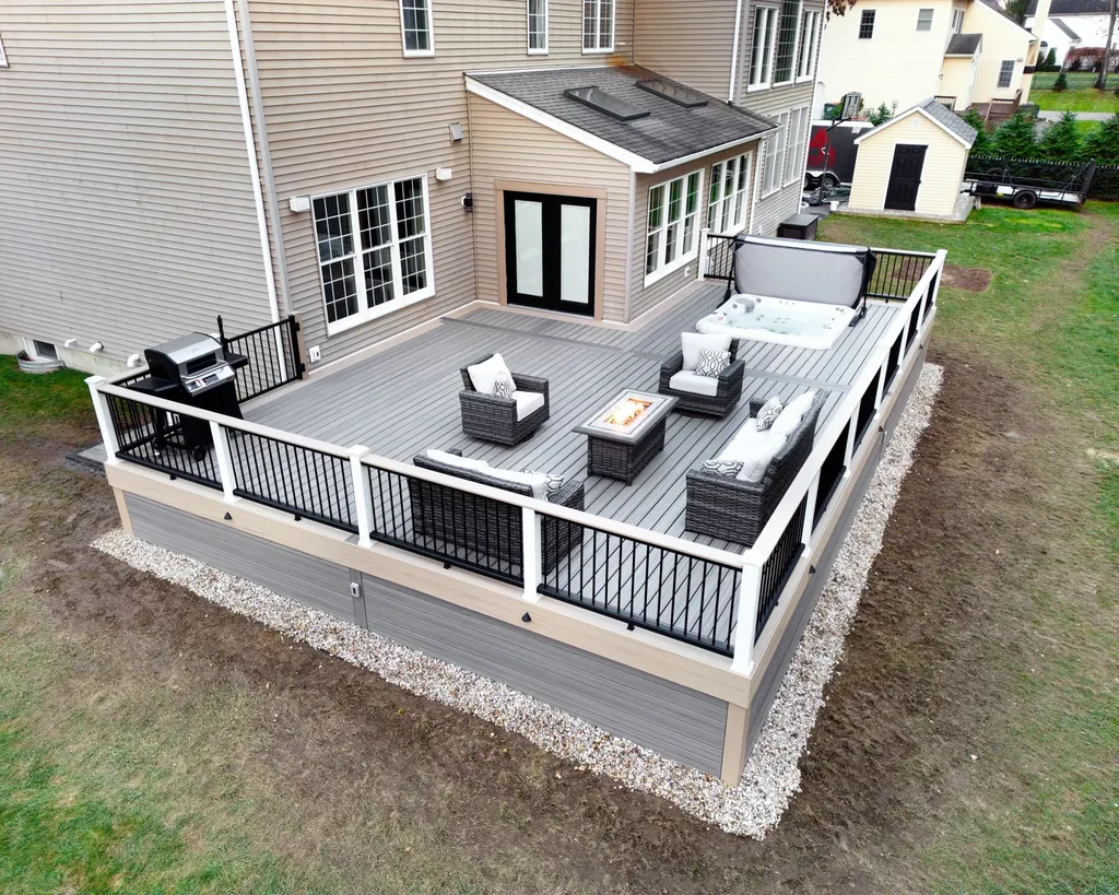 Aerial view of a gray deck with a hot tub, lounge seating, and a lit fire table