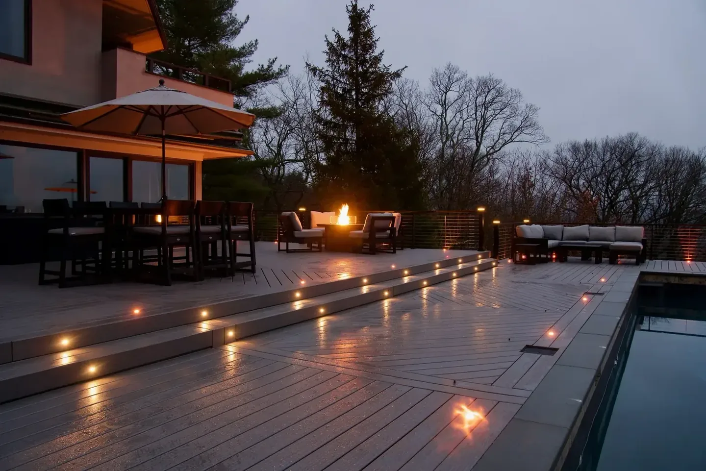 Covered deck with integrated lighting beside a pool at dusk