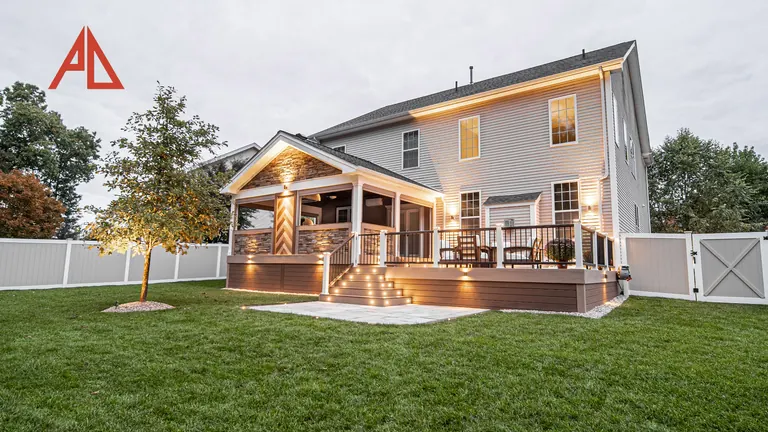 Covered porch and deck at dusk with lit stairs and a paver pad