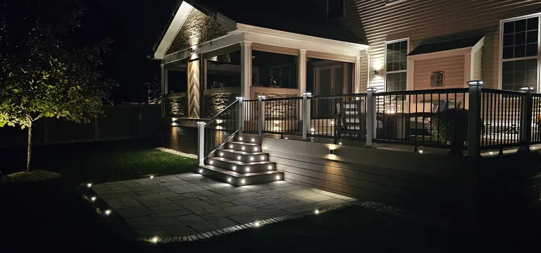 Covered deck and lit stairs down to a stone patio at night