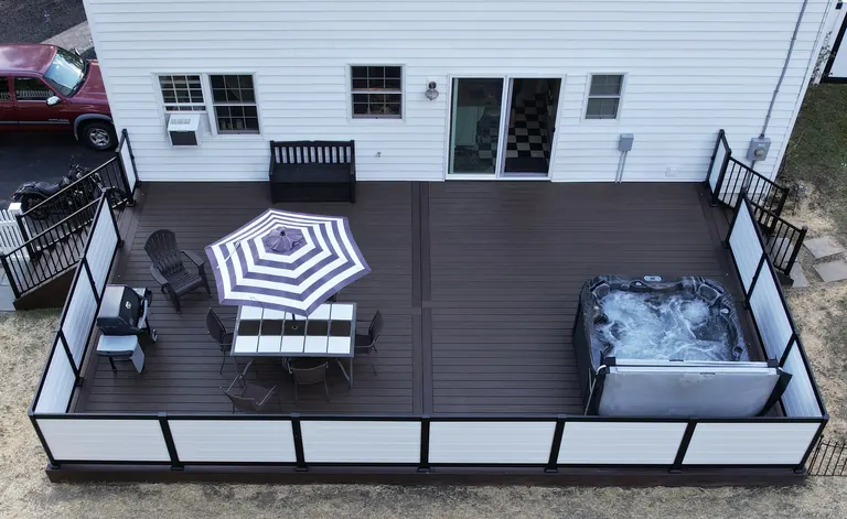 Aerial of a dark deck with a hot tub, dining under an umbrella, and white railing