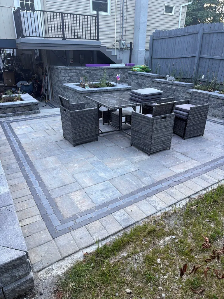 Wide patio shot of wicker furniture set on a herringbone paver patio next to a stone retaining wall, Rhinebeck, NY