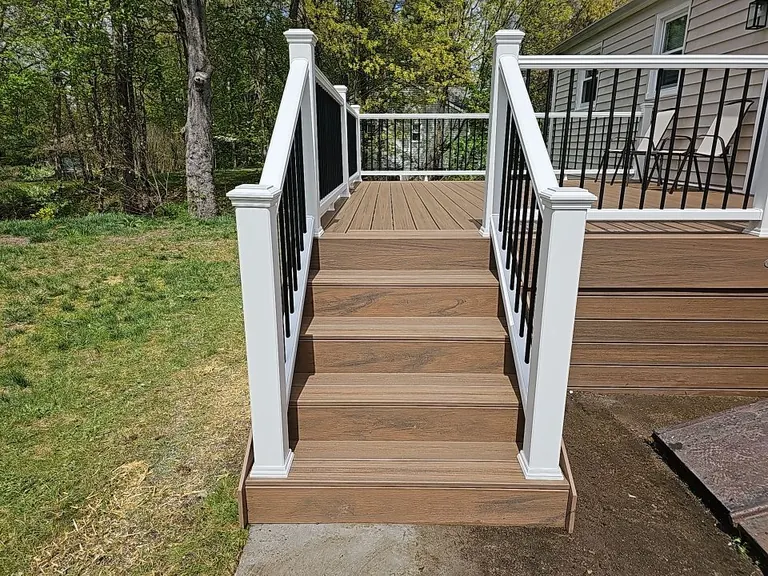 Finished composite deck stairs framed by white railing with black balusters, leading down to a paver landing, New Paltz, NY