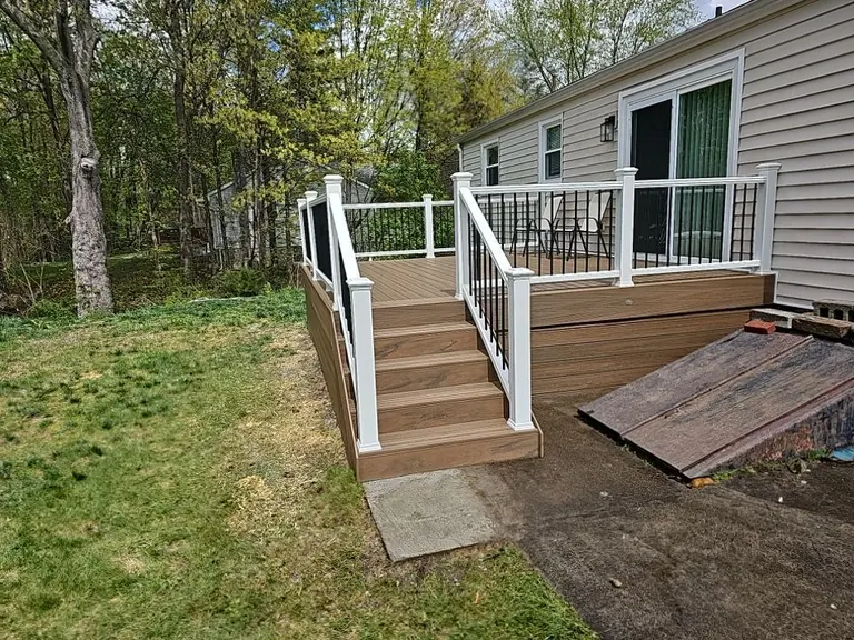 Angled view of a finished deck and entry stairs against a backyard tree line, white railing with black balusters, New Paltz, NY