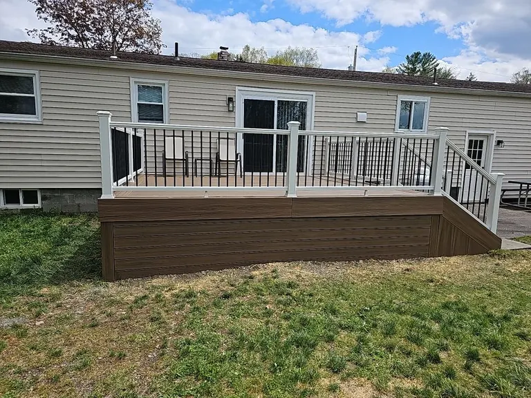 Rear view of a single-story home with a finished deck, white railing with black balusters, seating area near the door, New Paltz, NY