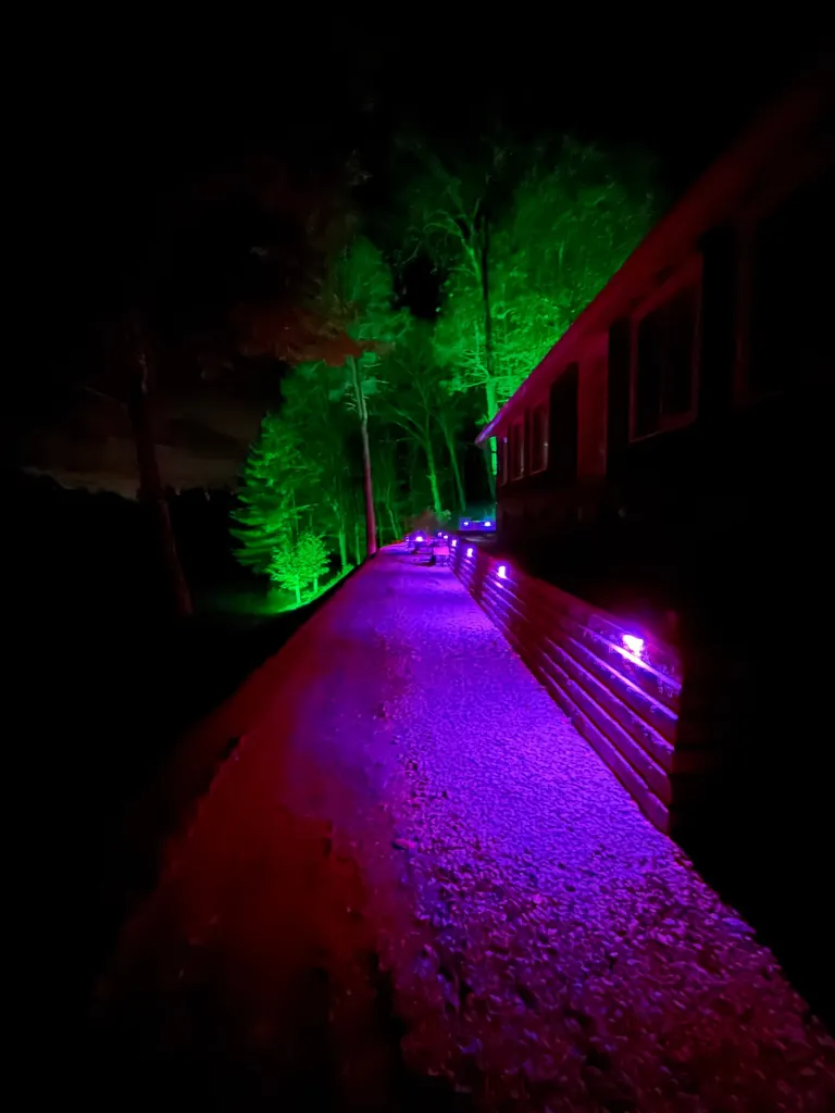 Night shot of a finished terraced stone retaining wall and pathway lit with multicolor accent lighting, trees in background, Boiceville, NY
