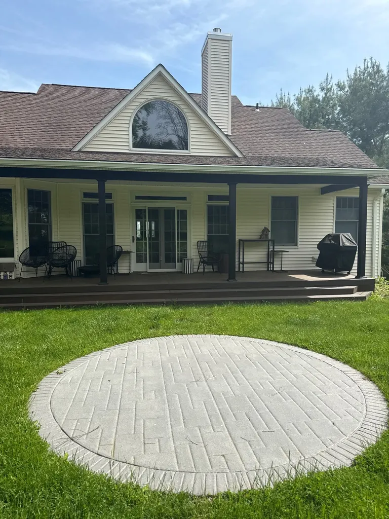 Wide rear view of a farmhouse with a finished covered porch, black posts, and a round paver patio on the lawn, Hyde Park, NY