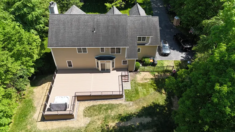 Aerial of full finished rear deck with hot tub, stairs, and rail along a wooded yard, Lagrangeville, NY