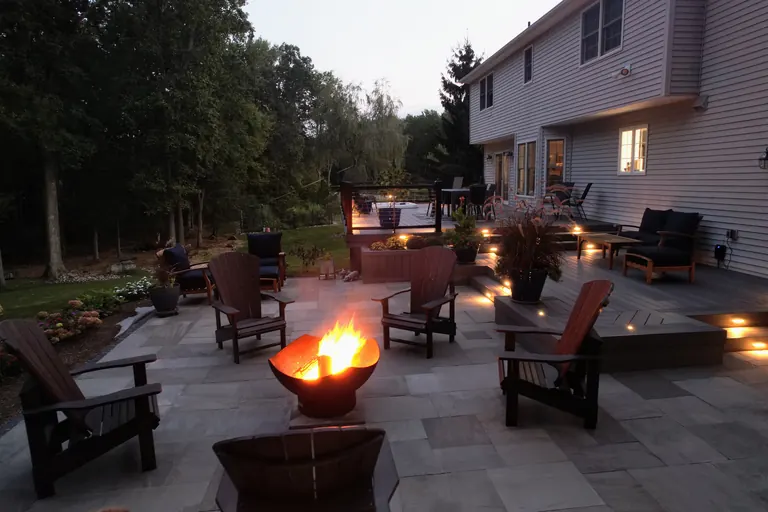 Twilight patio with fire pit, Adirondack chairs, and lit deck steps behind