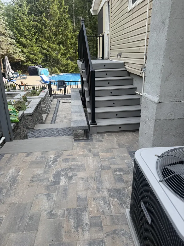 Composite deck stairs with black aluminum railing leading up to house, patio and pool below
