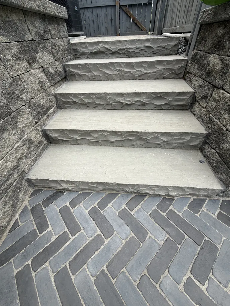 Stone paver steps with dark herringbone paver landing leading to a gated side yard