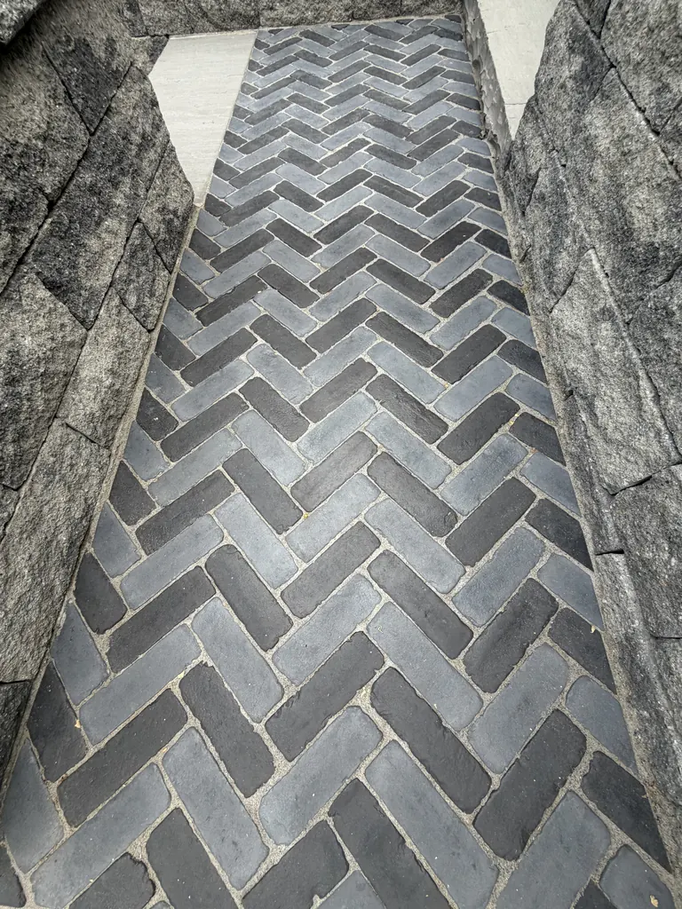 Close-up of dark herringbone-pattern paver walkway inset next to stone-capped retaining wall