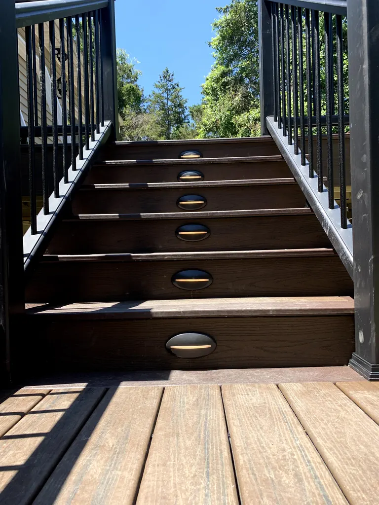 Daytime shot looking down composite deck stairs between black aluminum railings to trees and sky