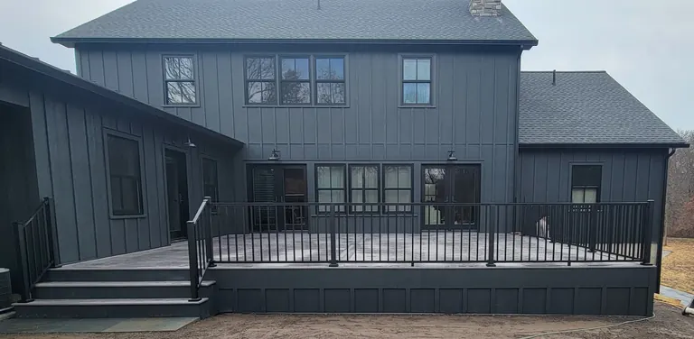 Finished composite deck with black aluminum railing against a dark modern board-and-batten house