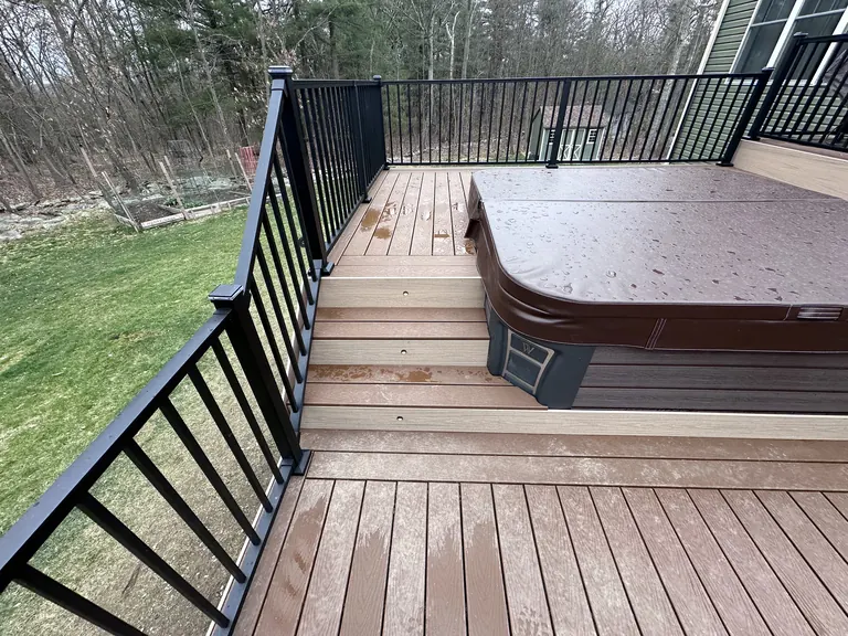 Hot tub with steps and black metal railing, deck level view