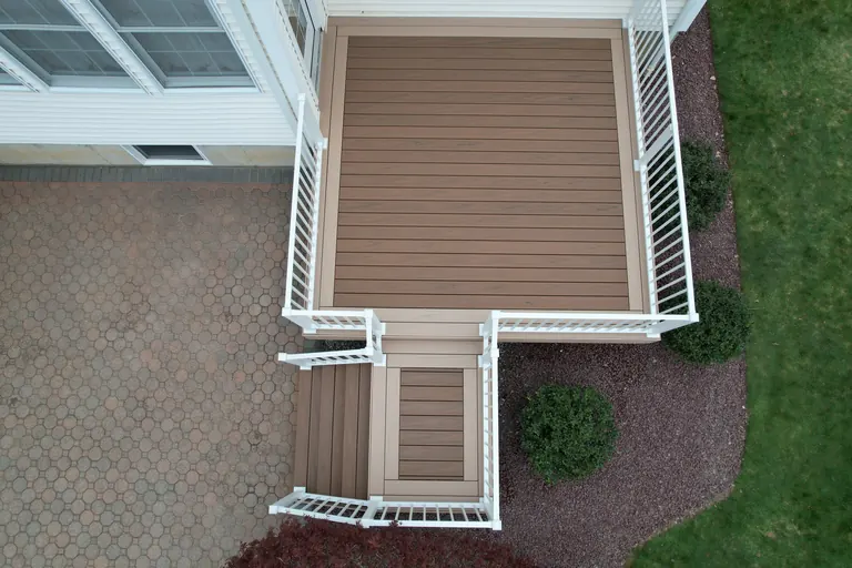Aerial daytime detail of a small finished deck landing with white railing next to a paver patio