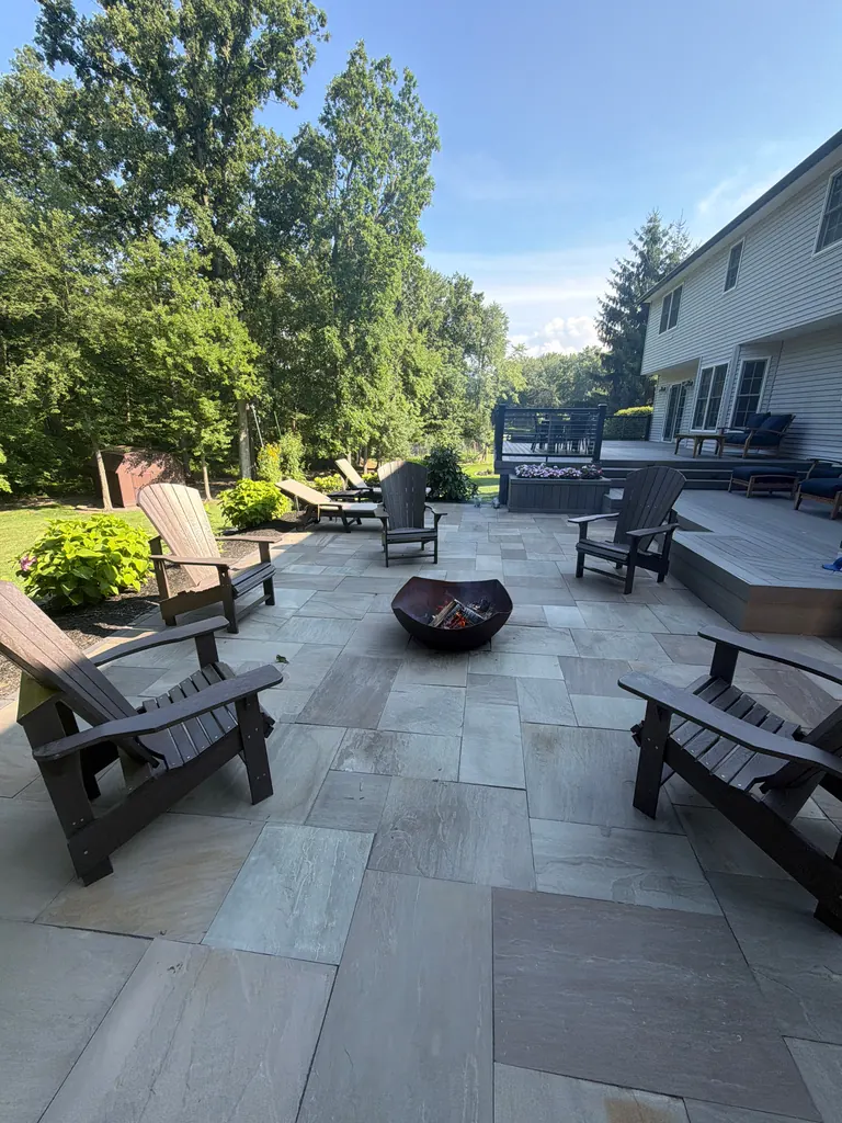 Daytime stone patio with Adirondack chairs around a fire pit, deck and house behind