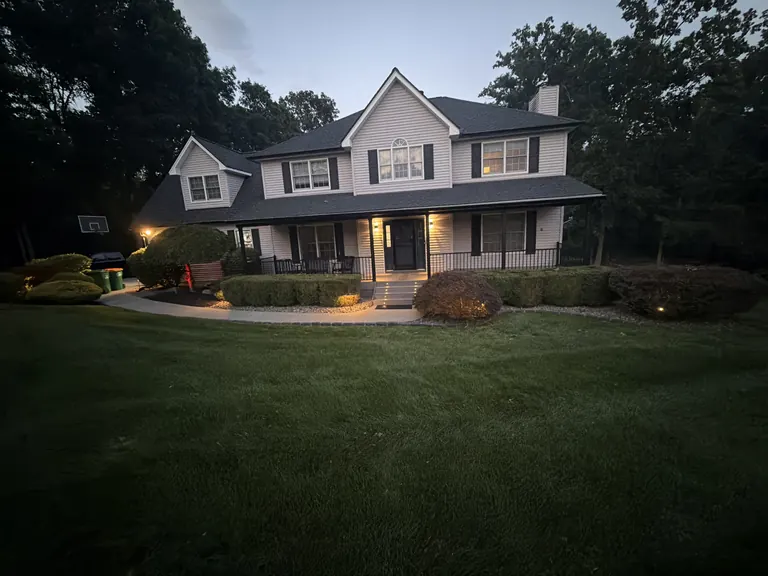 Twilight front of house with lit covered porch and landscape lighting