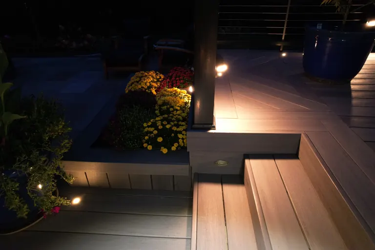 Night close-up of deck planter box, built-in step lighting, and herringbone deck pattern