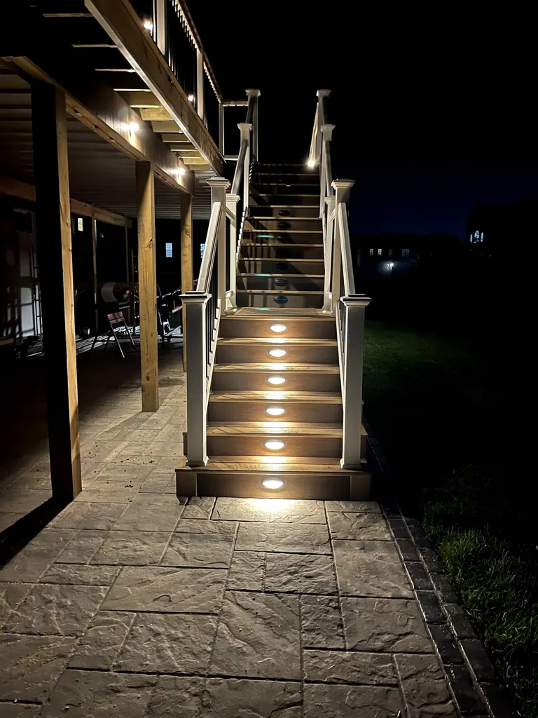 Night shot of composite deck stairs from house down to stone patio, LED riser lights lit on every step, Wappingers Falls, NY