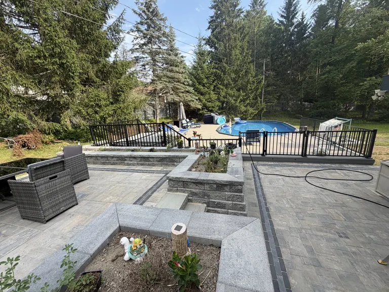 Raised bluestone-look paver patio with granite seat walls and planters, steps down to an in-ground pool deck, Dutchess County, NY