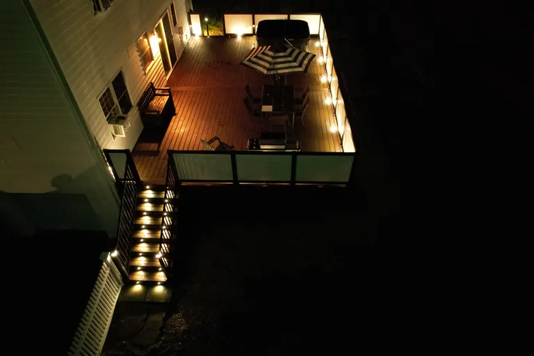 Night aerial view of the same composite deck with lit stair risers, dining set, and umbrella, Dutchess County, NY