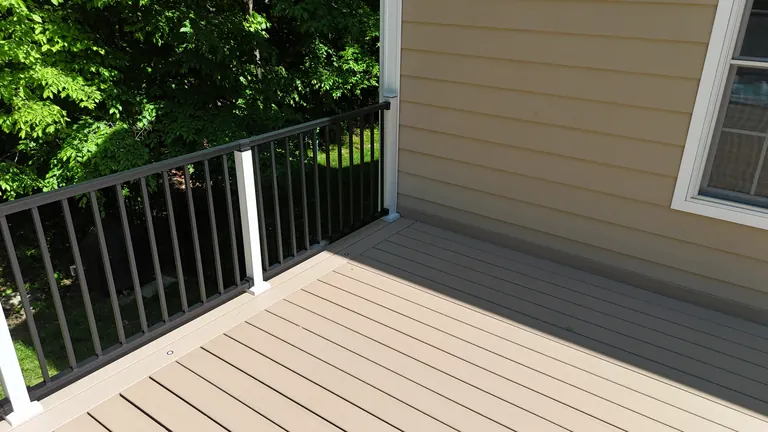 Deck corner detail, tan-gray decking against black baluster railing and yellow siding, Lagrangeville, NY