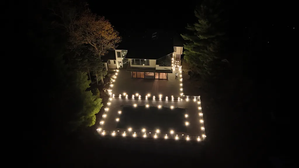 Night aerial of a deck and pool outlined by rows of warm lights beside a modern house