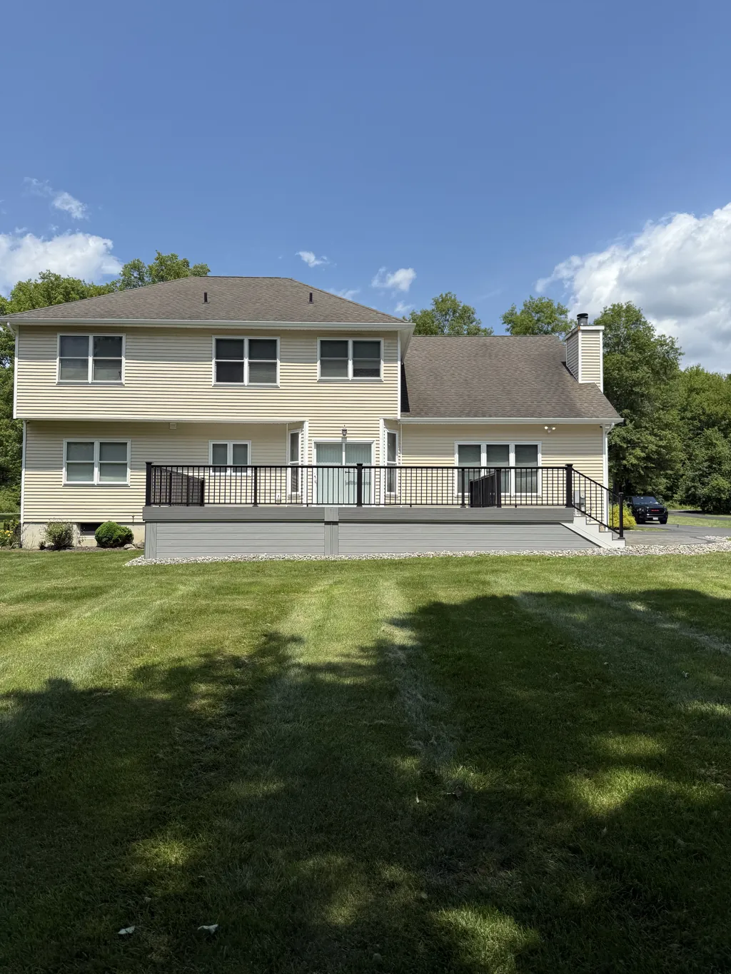 Rear elevation of a two-story colonial with a composite deck and black metal railing, summer lawn, Orange County, NY