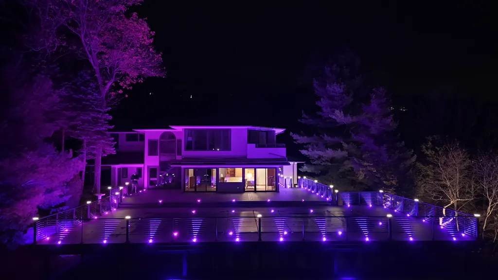 Night aerial of a house washed in purple light above decks lined with glowing rail lights