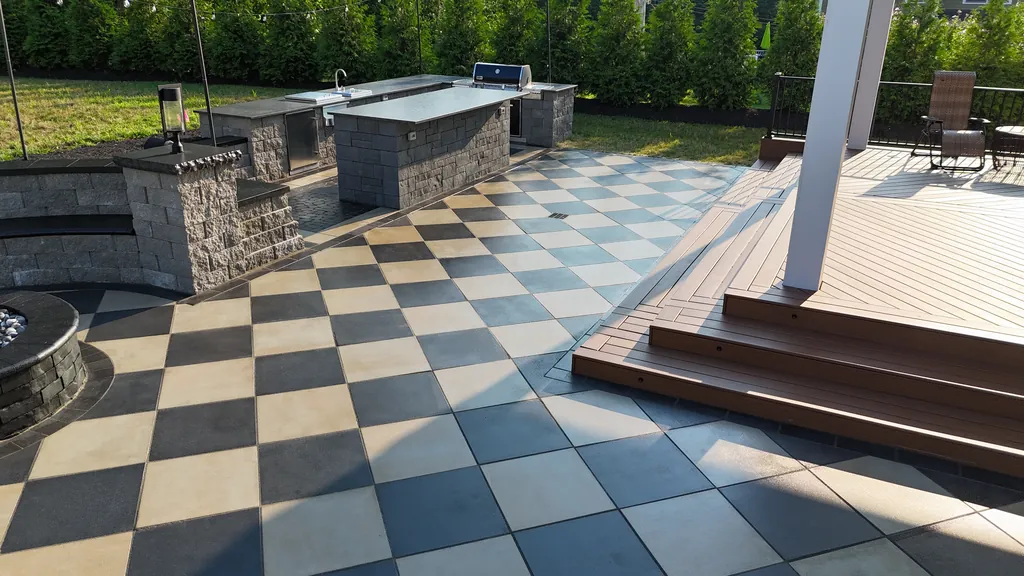 Wide composite deck steps down to a checkerboard patio beside a stone outdoor kitchen