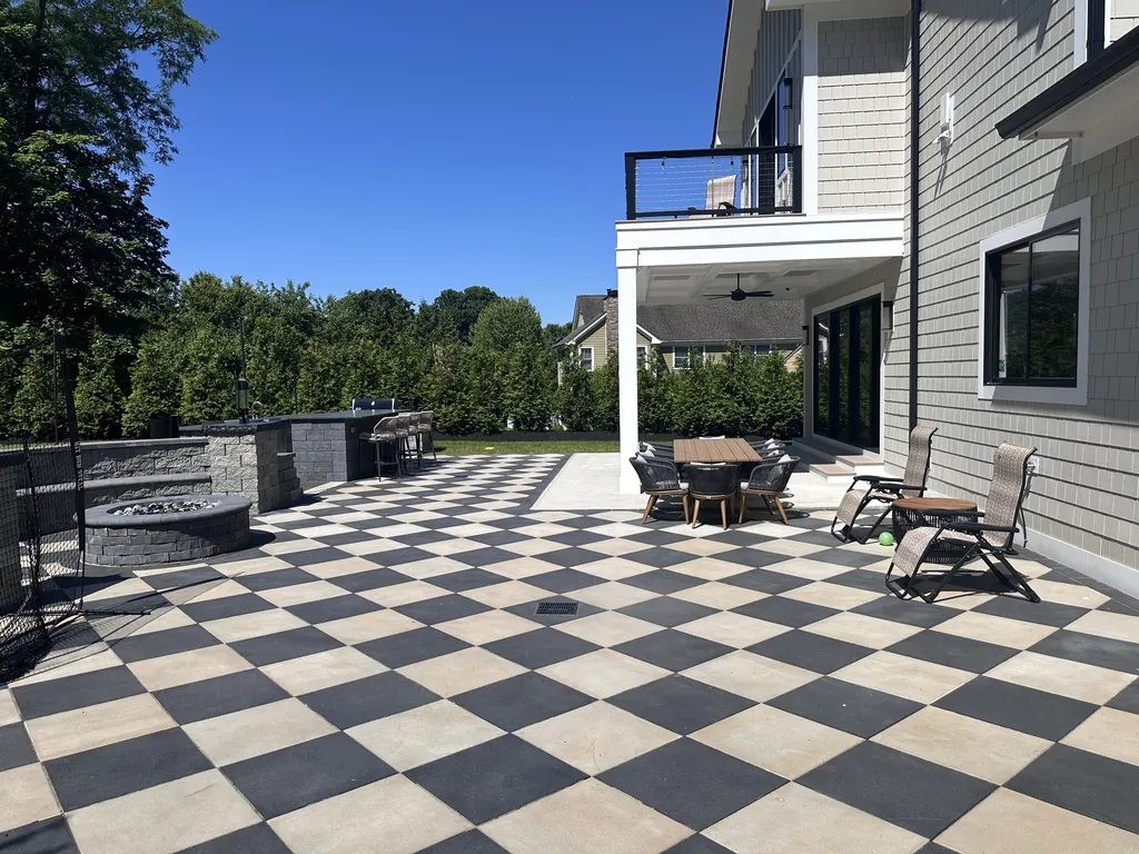 Checkerboard paver patio with a fire pit and dining set below a covered deck